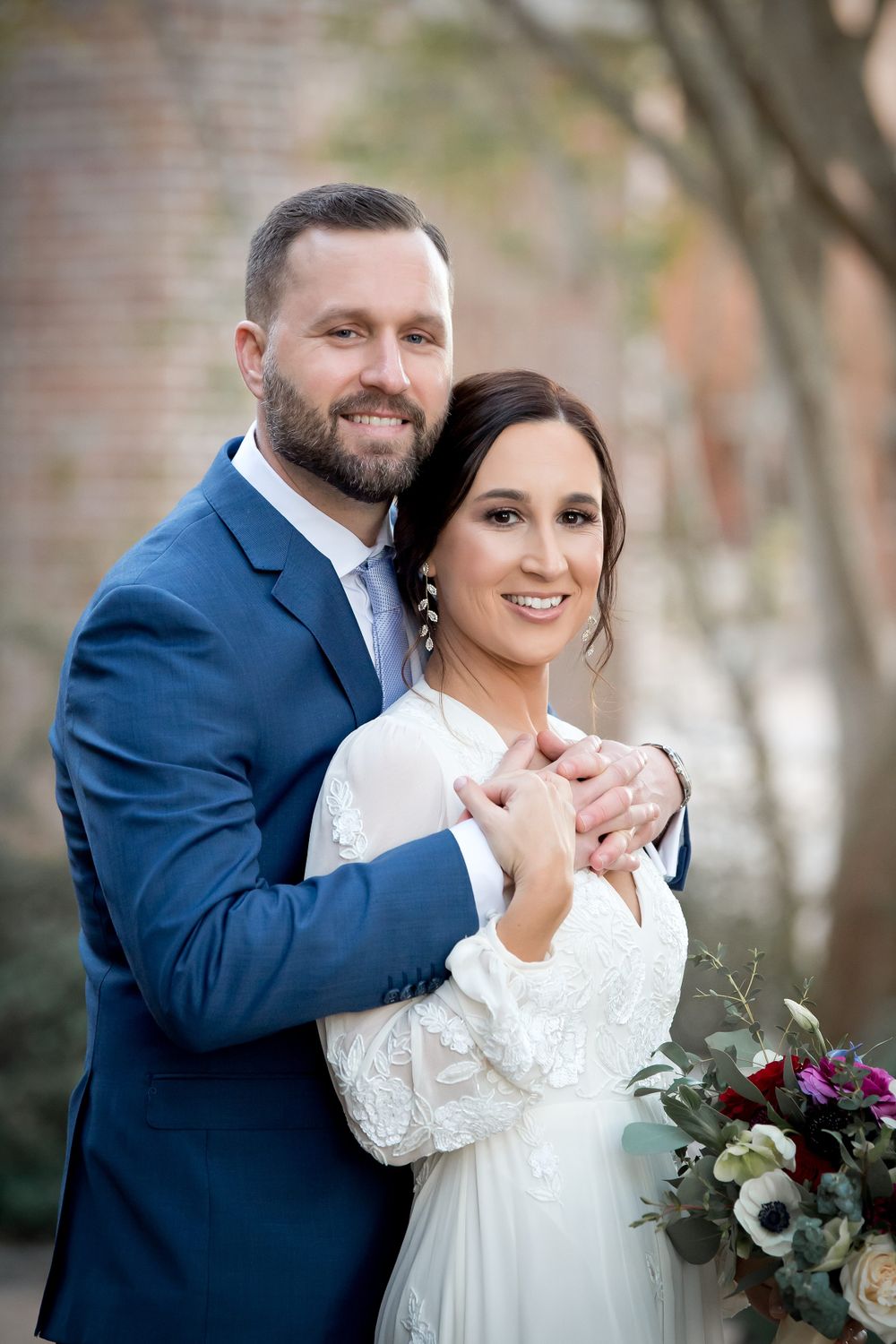 Couple embraces during their wedding first look photos by a brick wall.