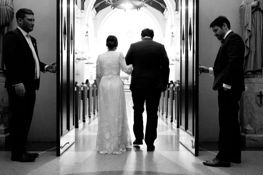 Wedding guests gather in a church hallway before the ceremony in black and white.