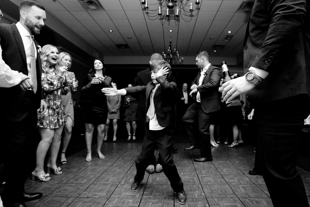 Wedding guests dancing and celebrating on a reception dance floor under dim lighting.