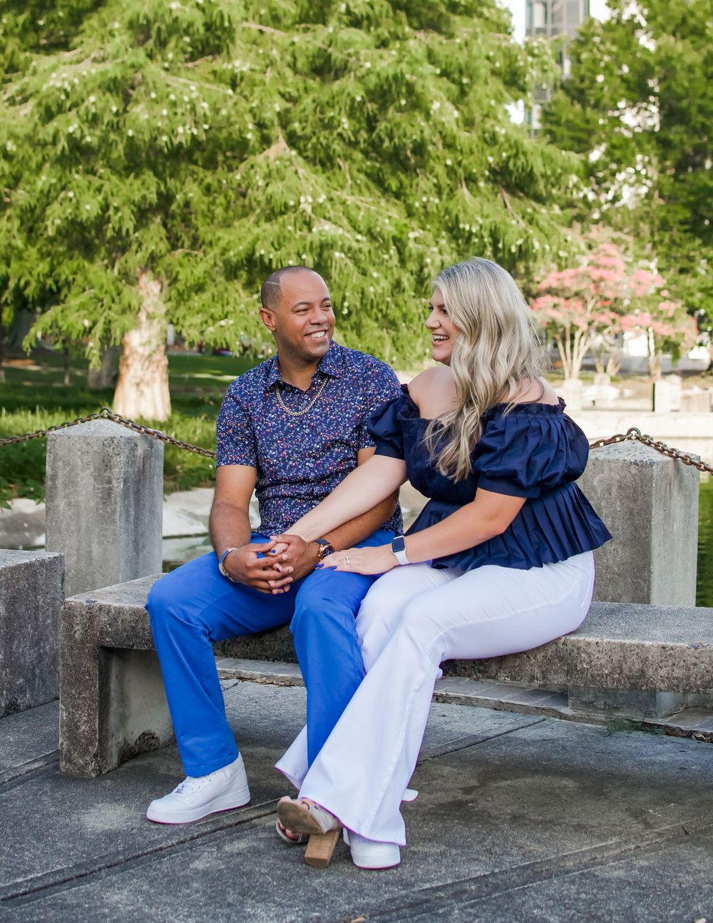A couple sitting on a stone bench. The man is holding the woman's hand in his lap and they are both smiling.
