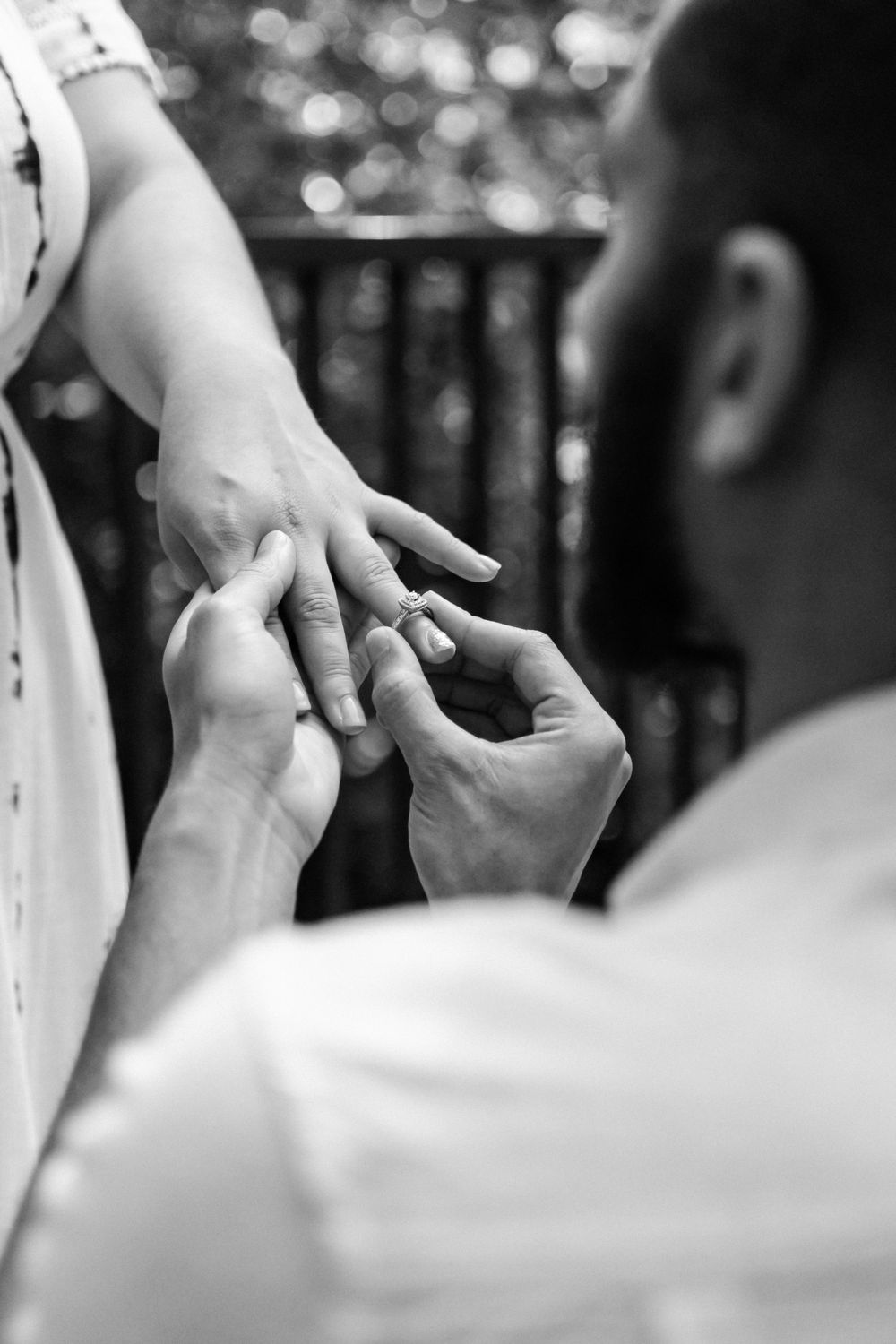 A black-and-white close-up photo of a man putting an engagement ring on a woman's finger.