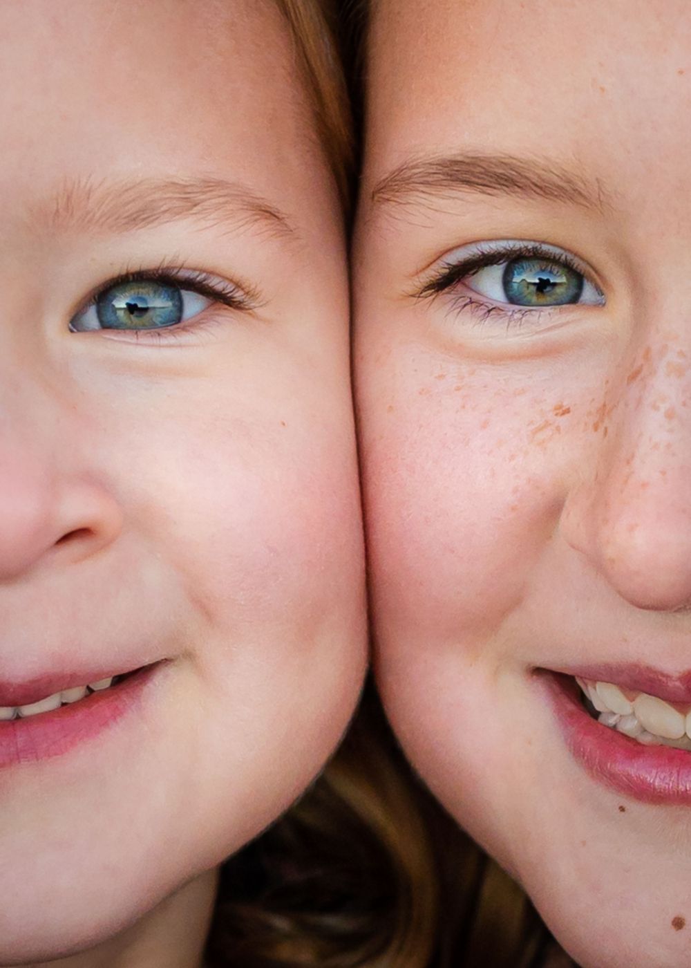 Two children's faces pressed together showing bright blue eyes and sweet smiles in closeup.