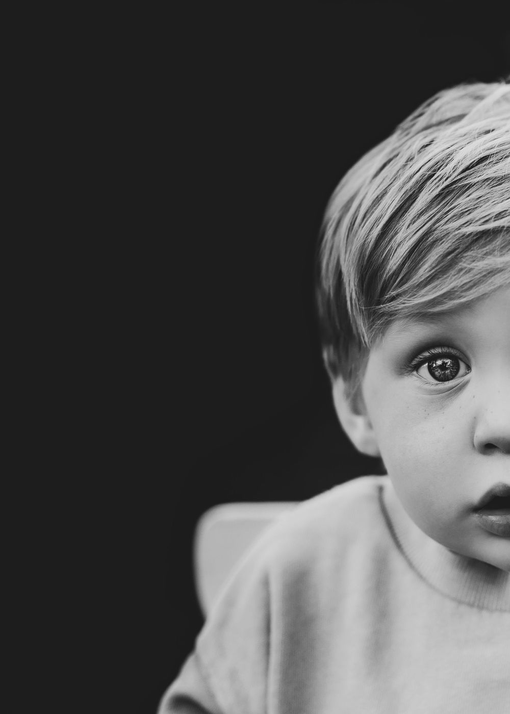 Black and white portrait of child with wide eyes against dark background.