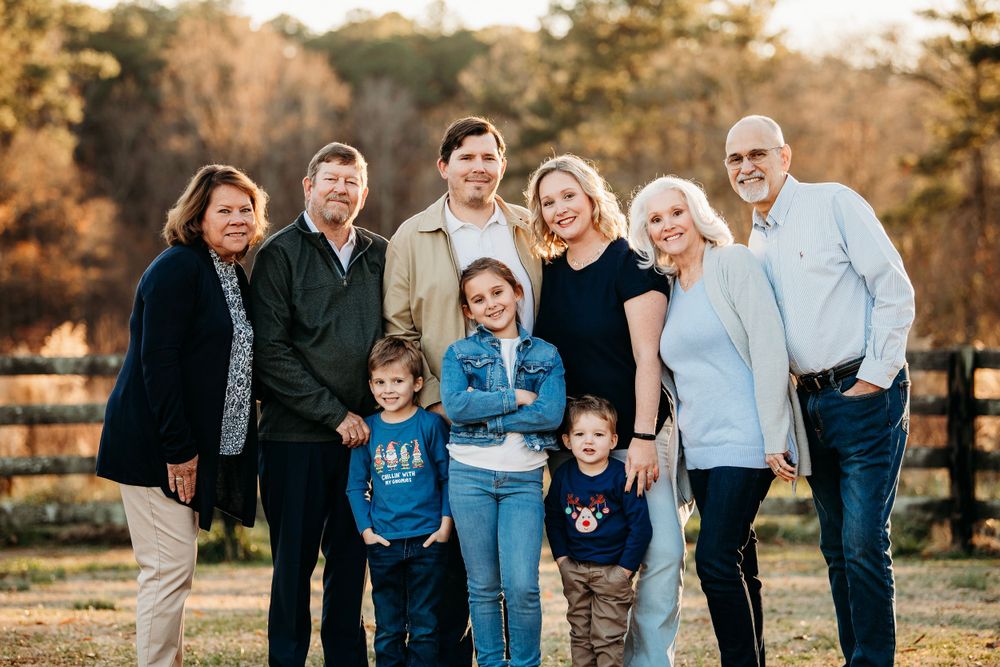 Multi-generational family portrait with grandparents, parents, and young children smiling outdoors at golden hour.