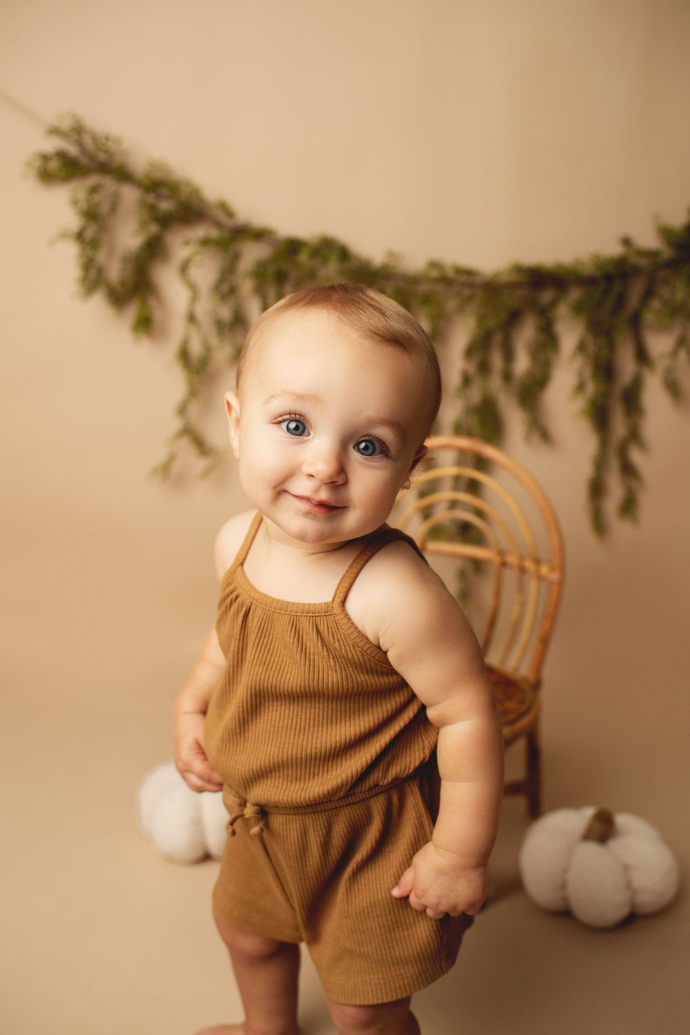 Adorable blue-eyed baby in brown romper smiling in front of fall pumpkin studio backdrop.
