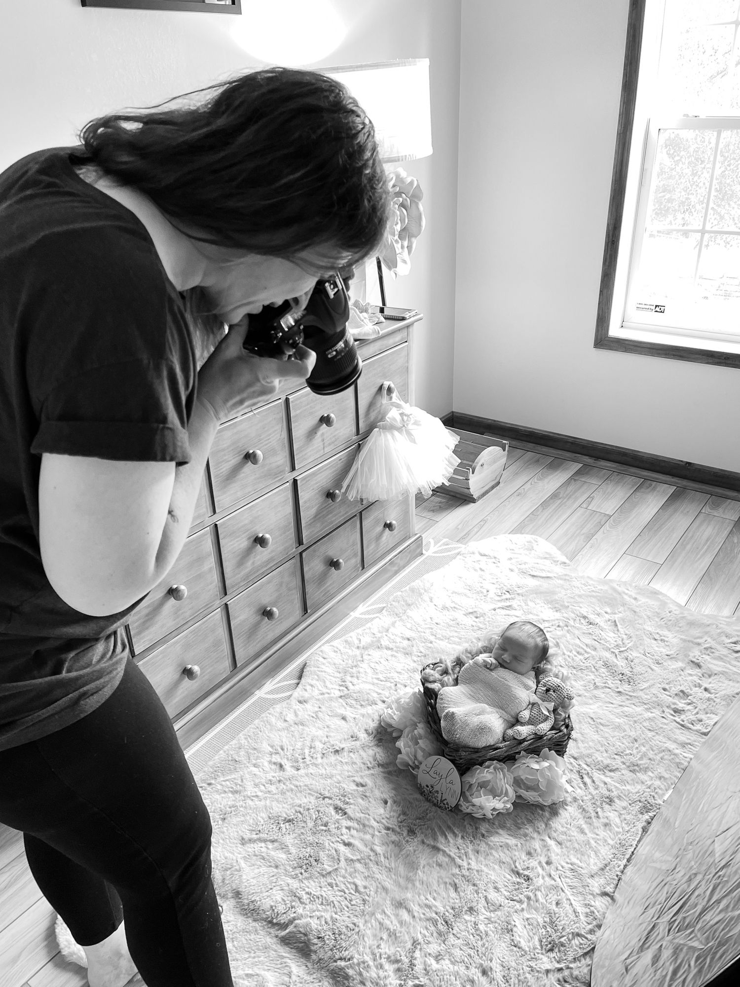 Person photographing a newborn photography setup on a white blanket with drawers in background.