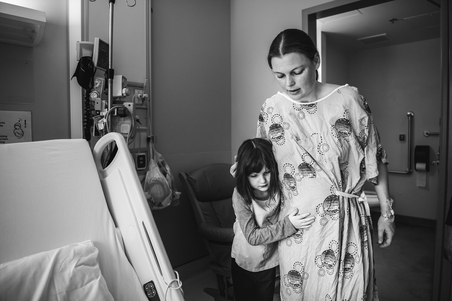 A young girl helps support her mother walk to her hospital bed after a cesarean birth.