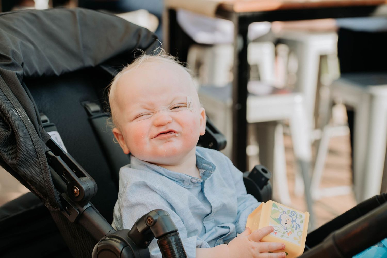 A baby sitting in a stroller while holding a snack.
