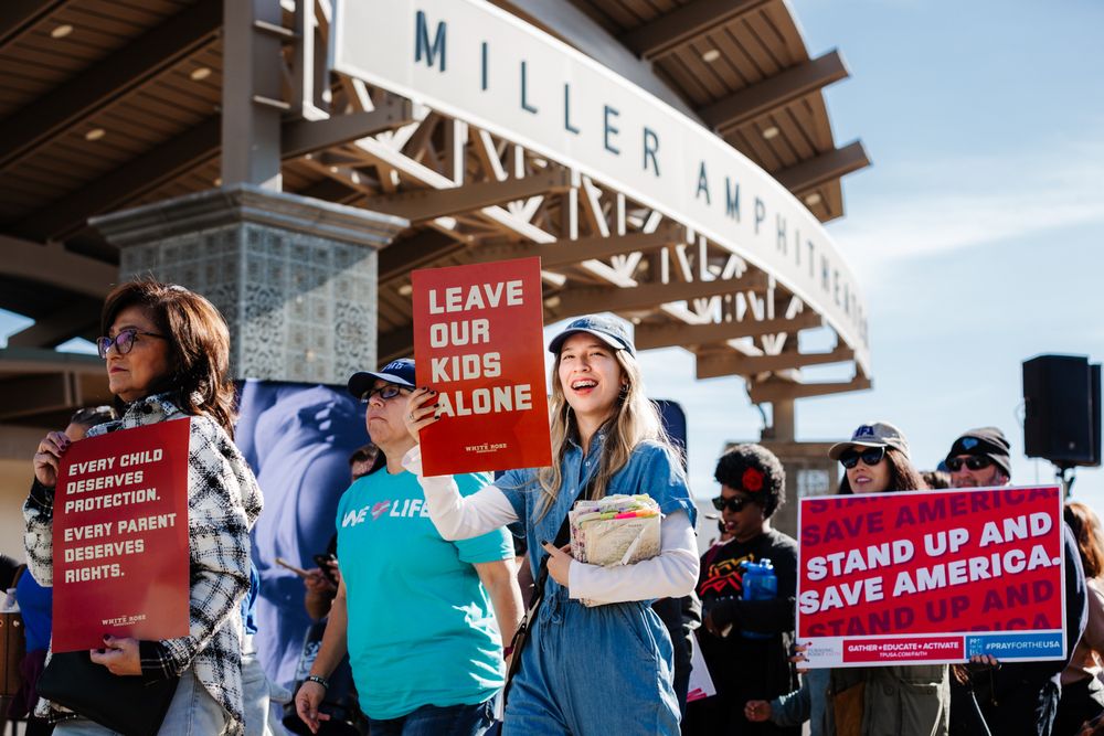 Crowd gathered outside Miller Arena holding protest signs and banners.