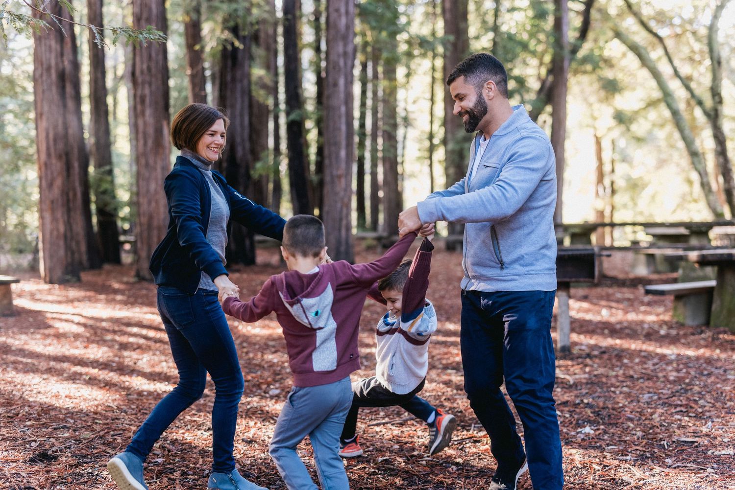 Family playing and spinning together on woodchip trail among tall redwood trees.