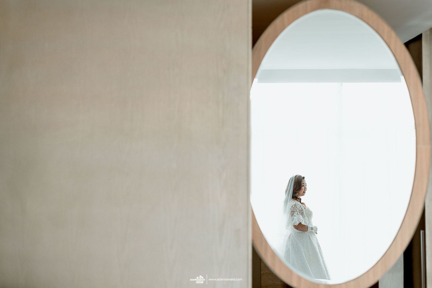 A bride's reflection is captured in a circular mirror against a minimalist backdrop.