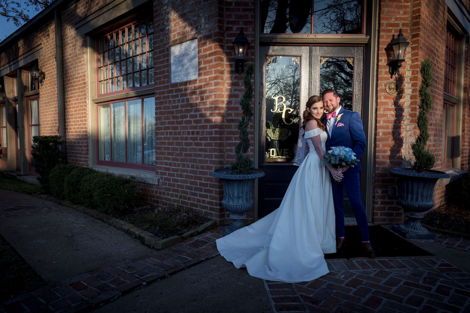 Evening wedding photos captured against brick building exterior with dramatic lighting.