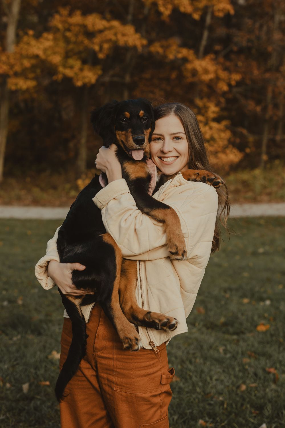 A joyful moment with a black and tan dog being held in a cream jacket and orange pants outdoors.