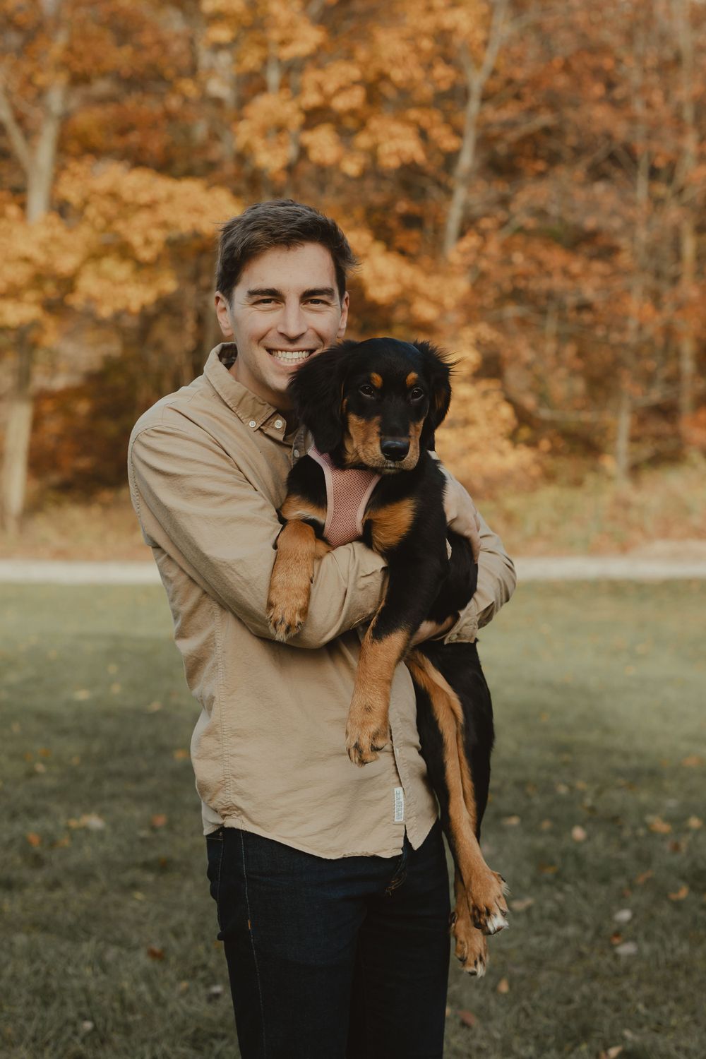 A joyful portrait of a person hugging their black and tan dog in a fall setting.