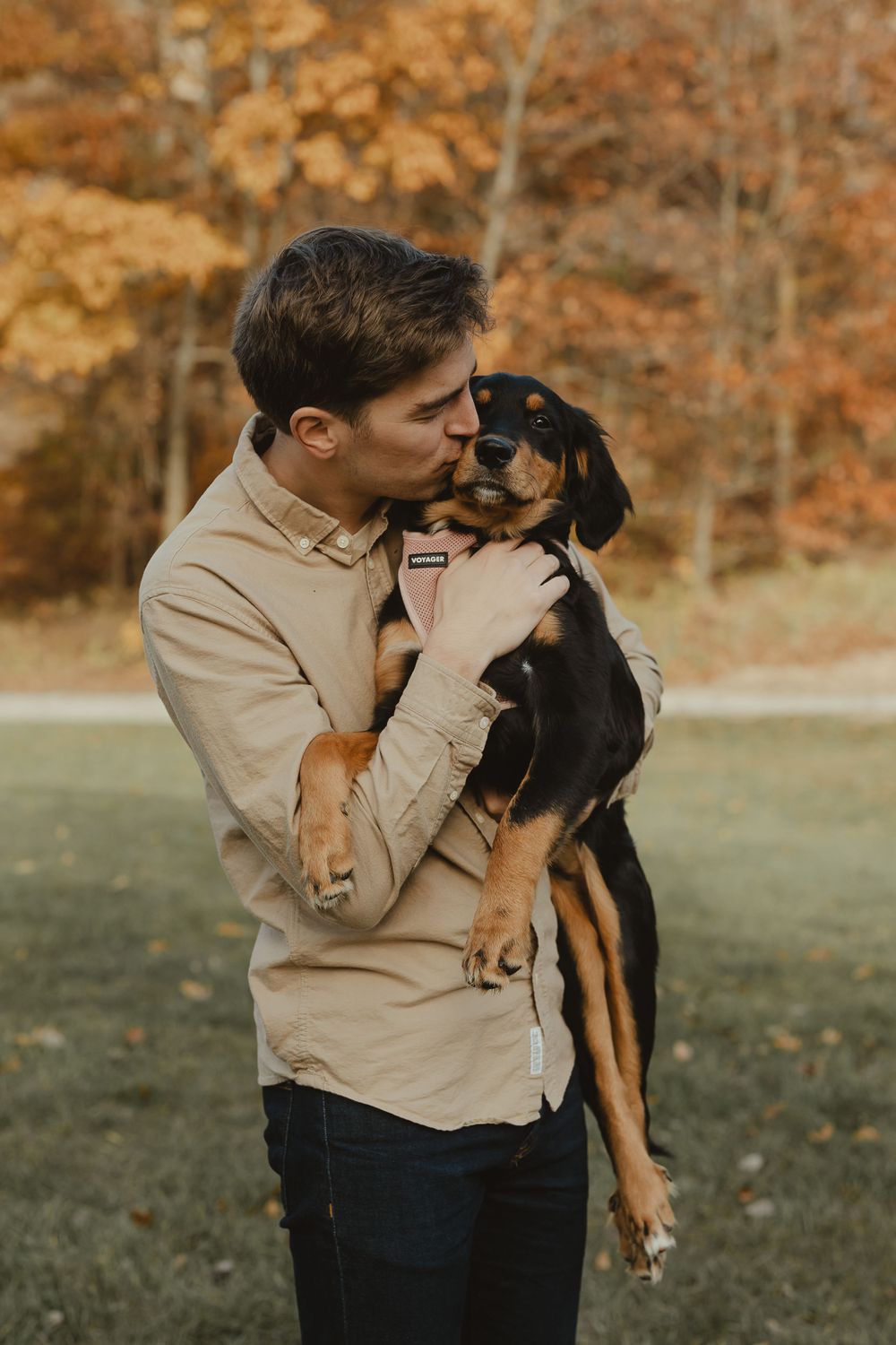 A tender moment between a person and their black and tan dog against fall foliage.