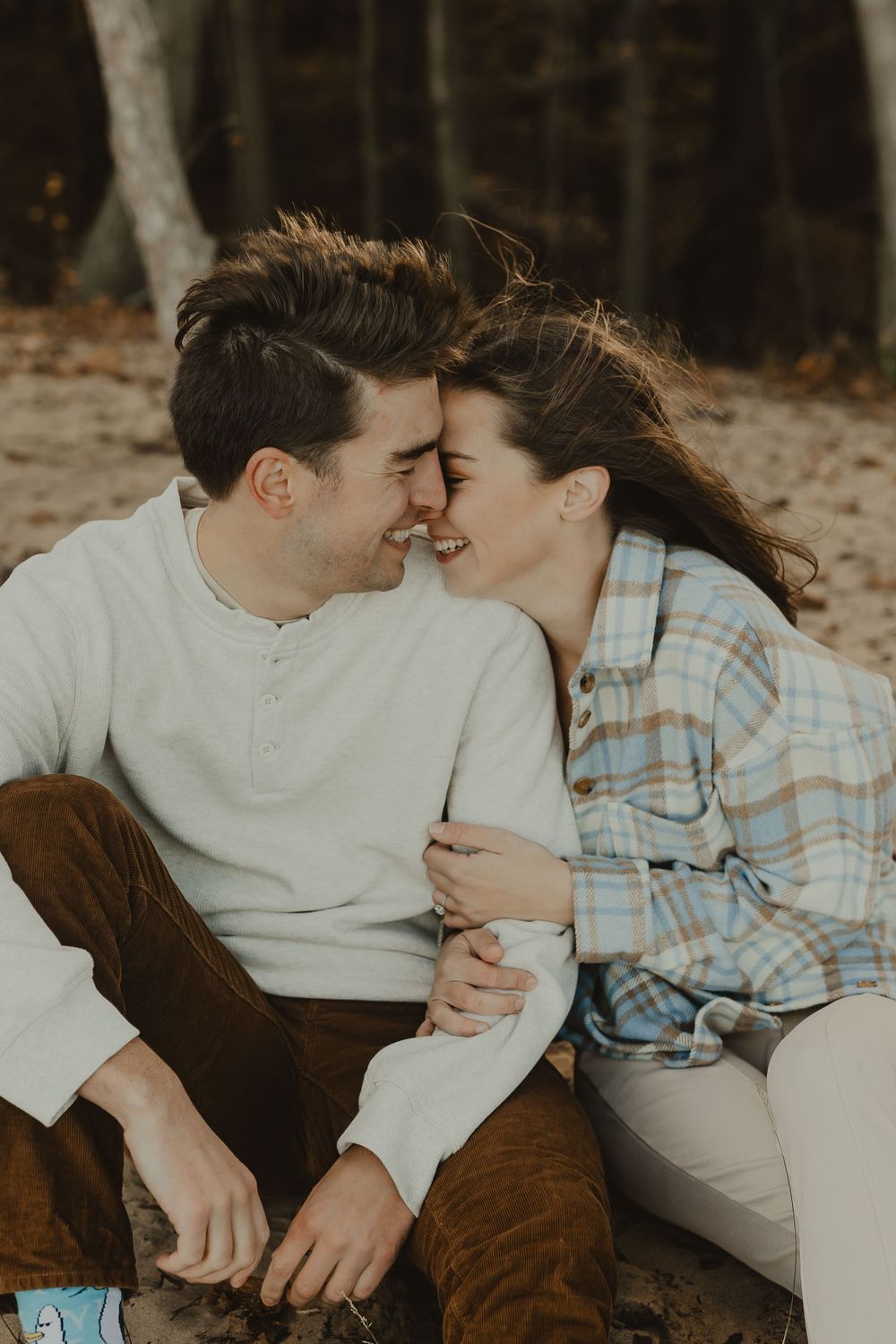 An intimate moment between a couple sitting close together surrounded by fallen autumn leaves.
