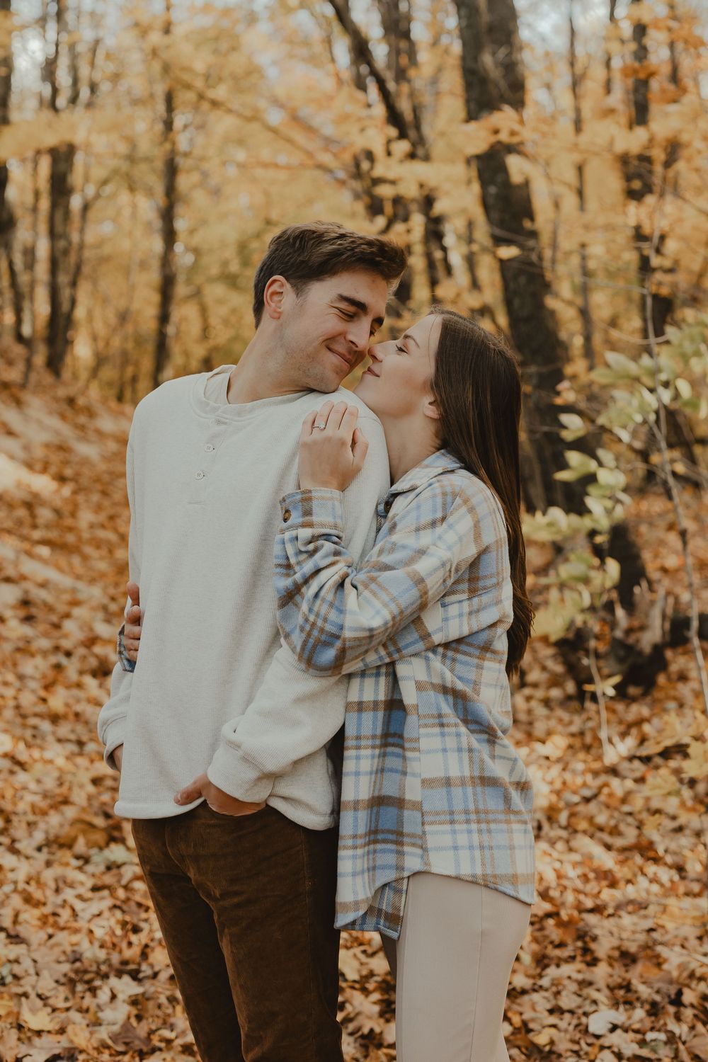 A romantic autumn photoshoot showing a couple embracing in a forest with golden fall foliage.