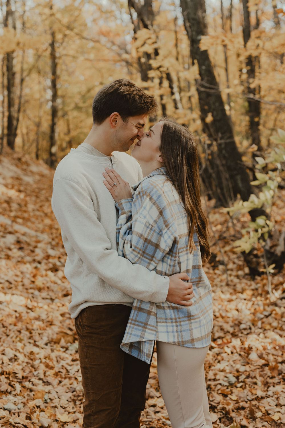 An intimate moment between a couple surrounded by golden fall foliage in the woods.