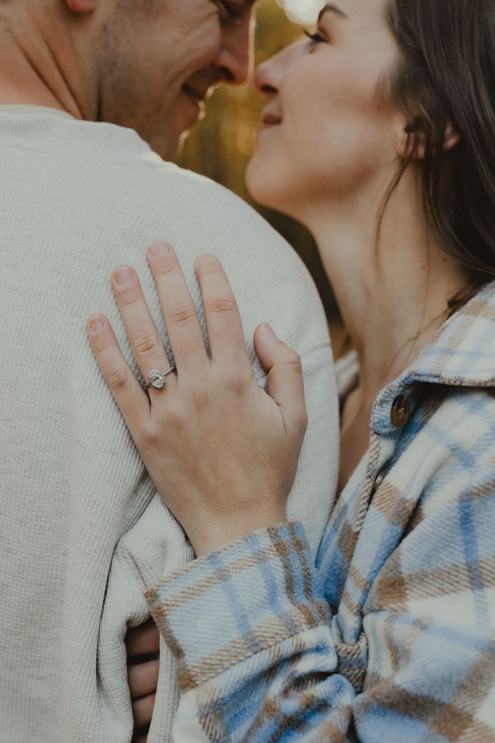 Close-up shot of an engagement ring as a couple shares an intimate moment in autumn attire.