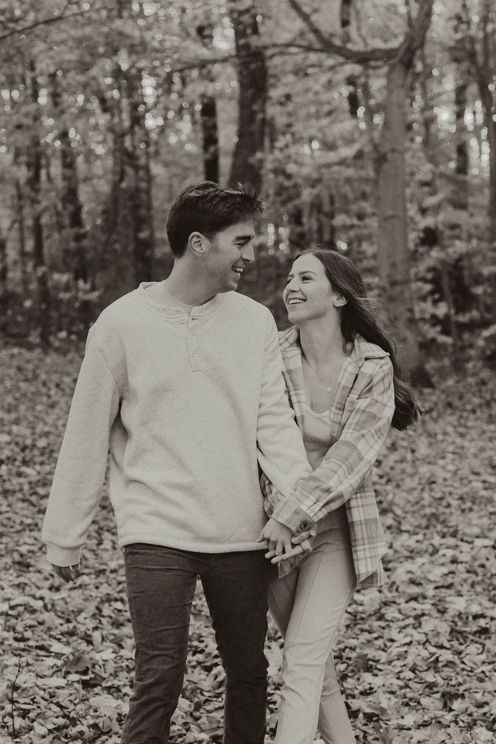 A couple shares a tender moment while walking through a forest filled with fallen autumn leaves.