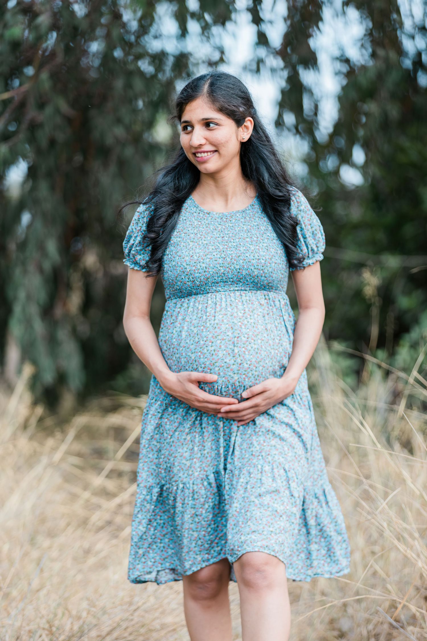 Maternity photo of woman in blue dress standing among tall grass.