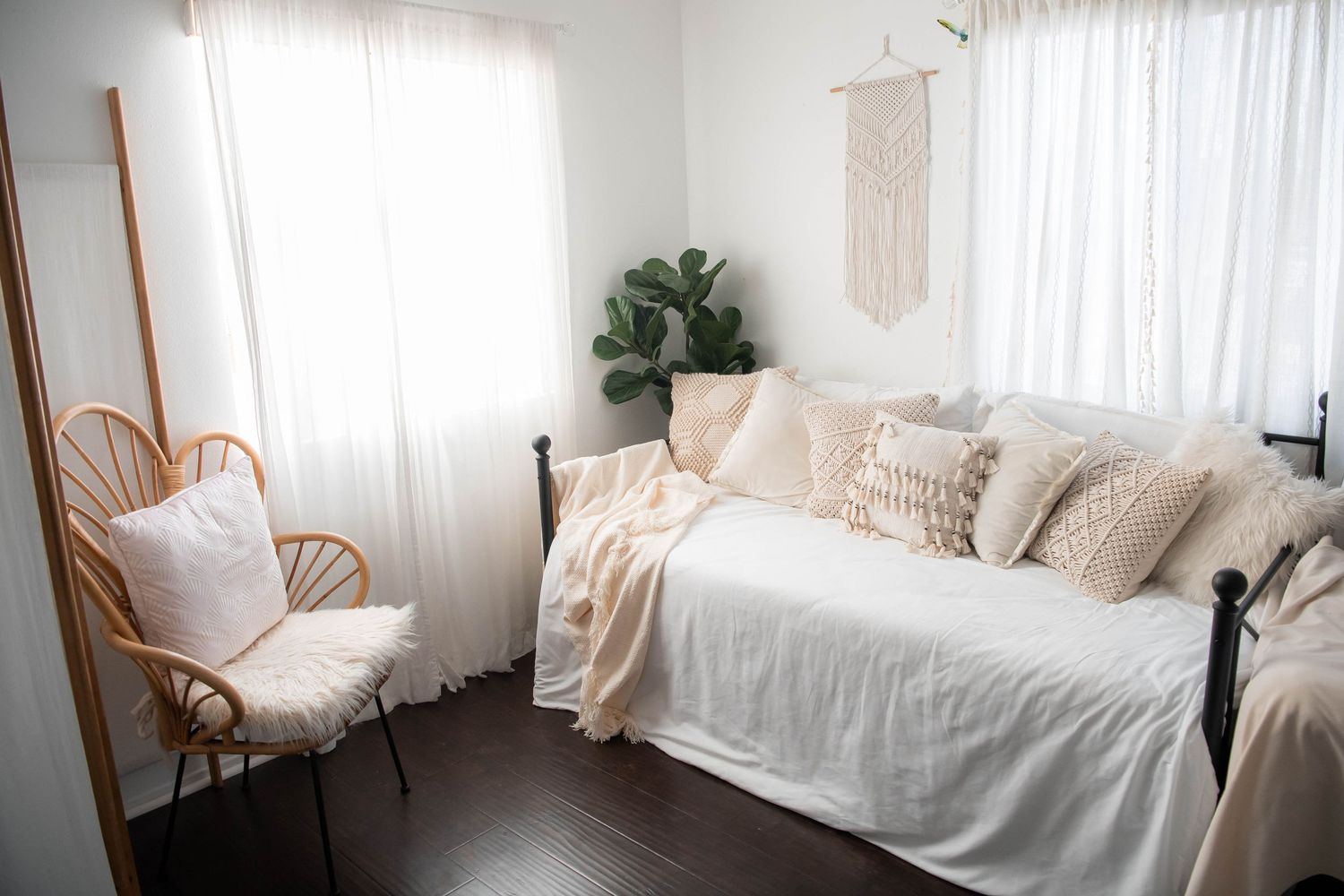 Minimalist boho bedroom with white daybed, rattan chair, and macrame wall hanging.
