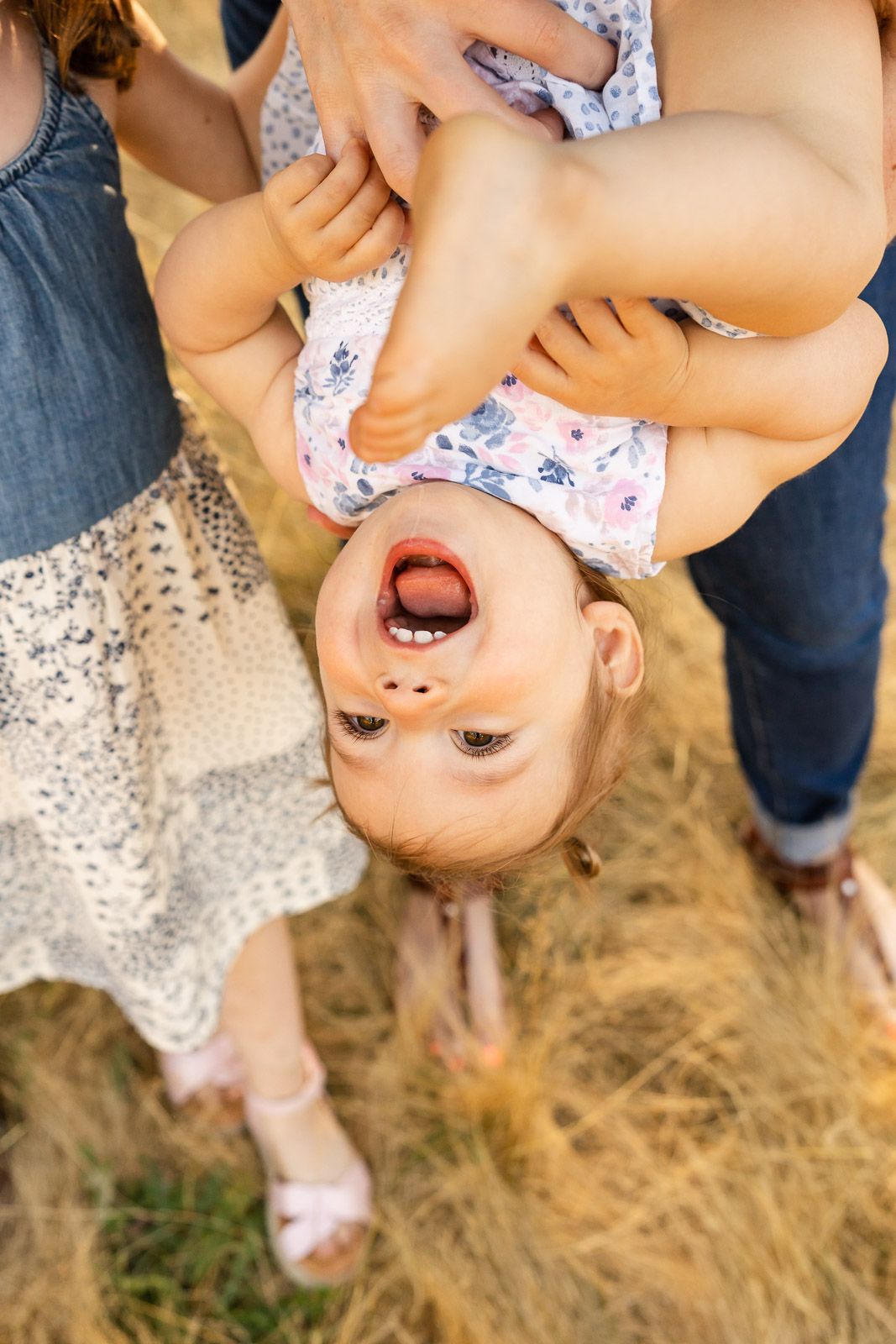 Little girl smiling joyfully while being flipped upside down.
