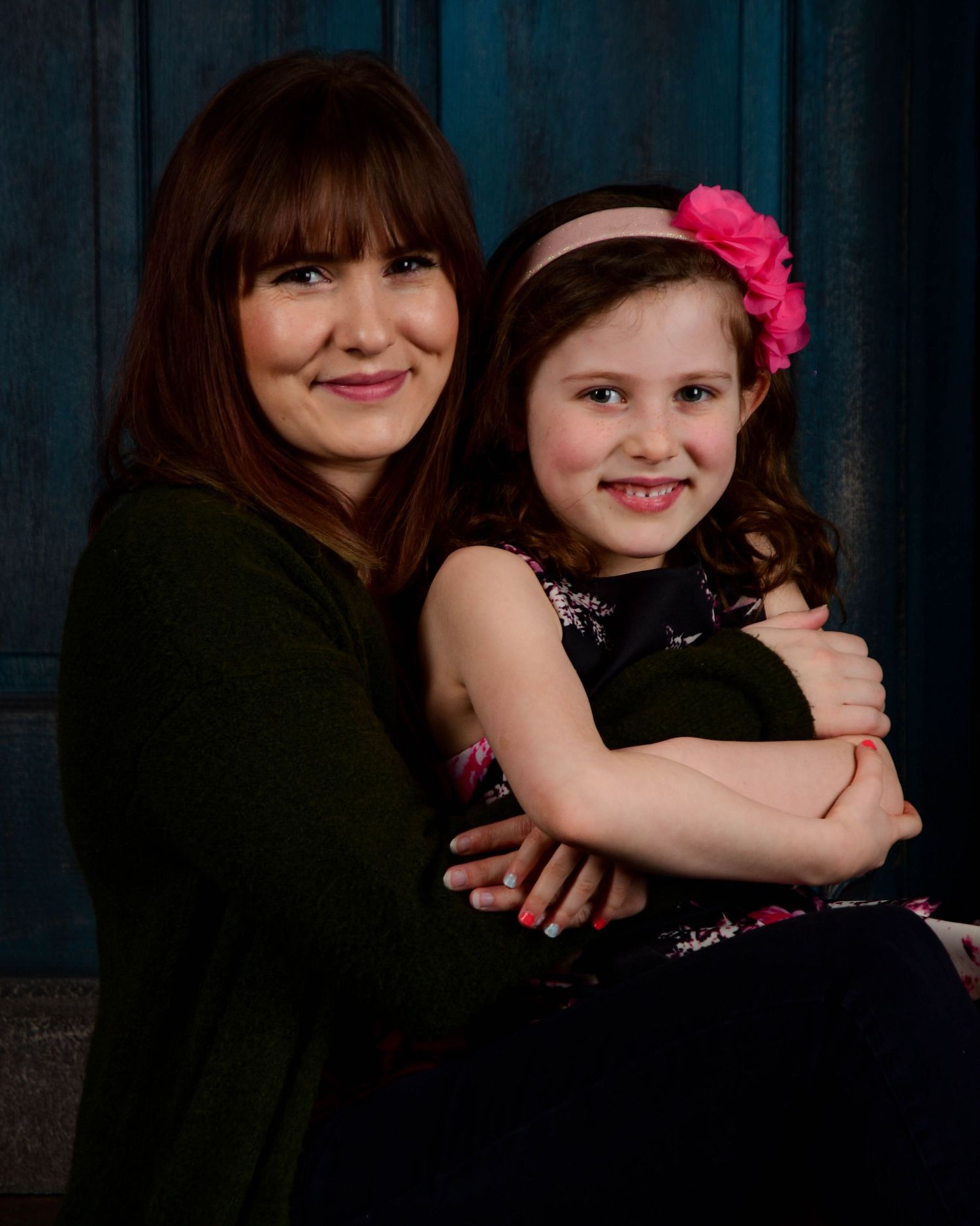 Mother and daughter share loving embrace in dark studio portrait series.