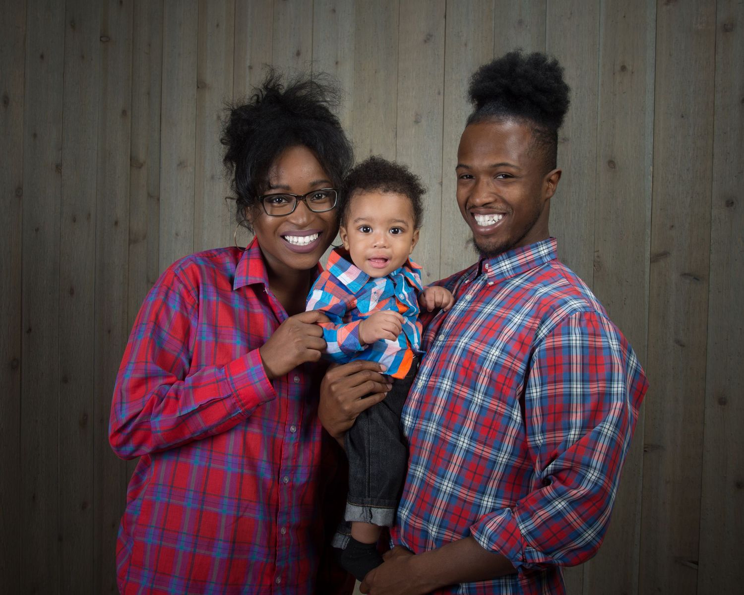 Family group wearing coordinated red plaid shirts posing against wooden wall.