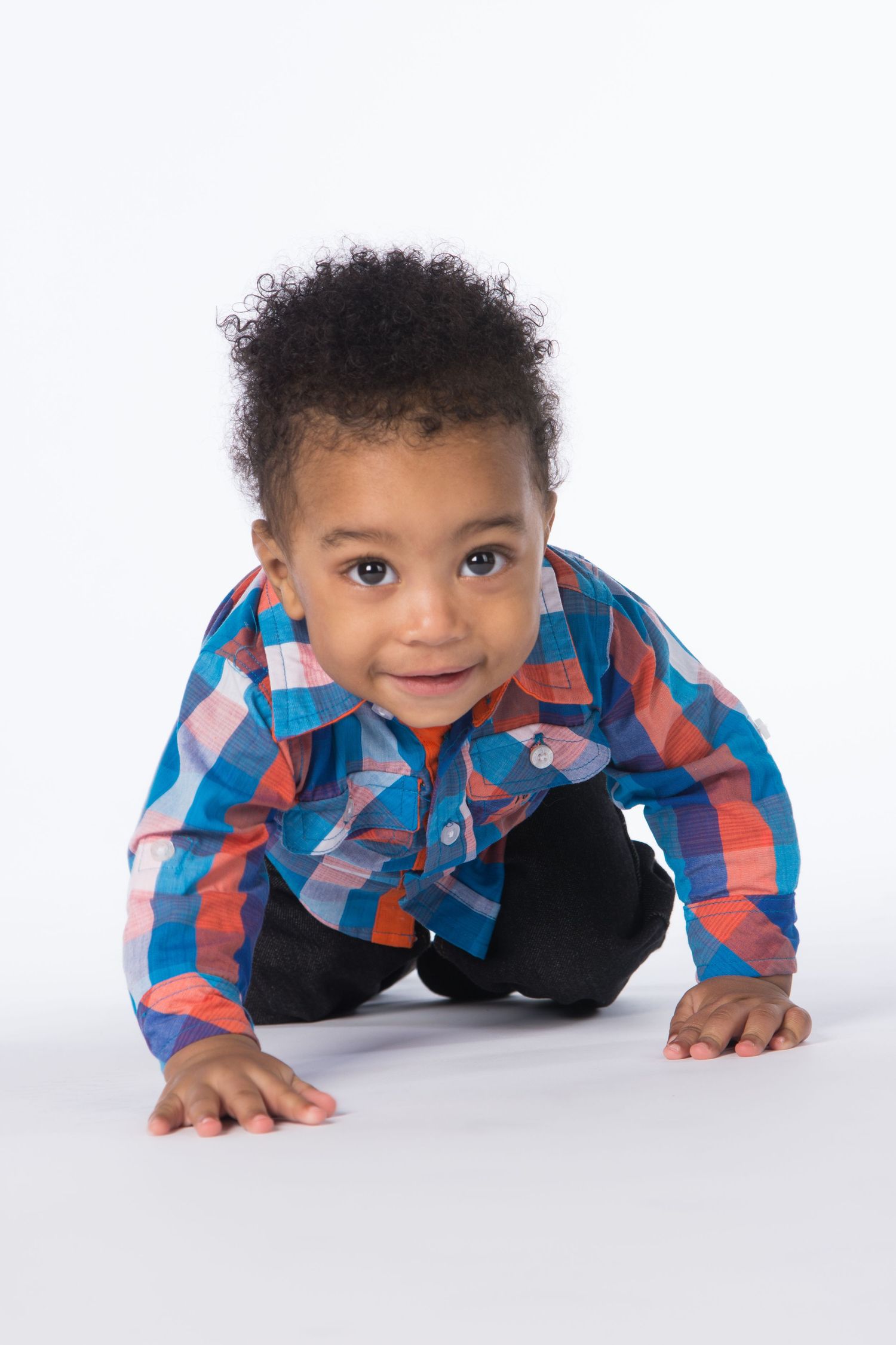Young child in plaid shirt crawling on white studio floor.