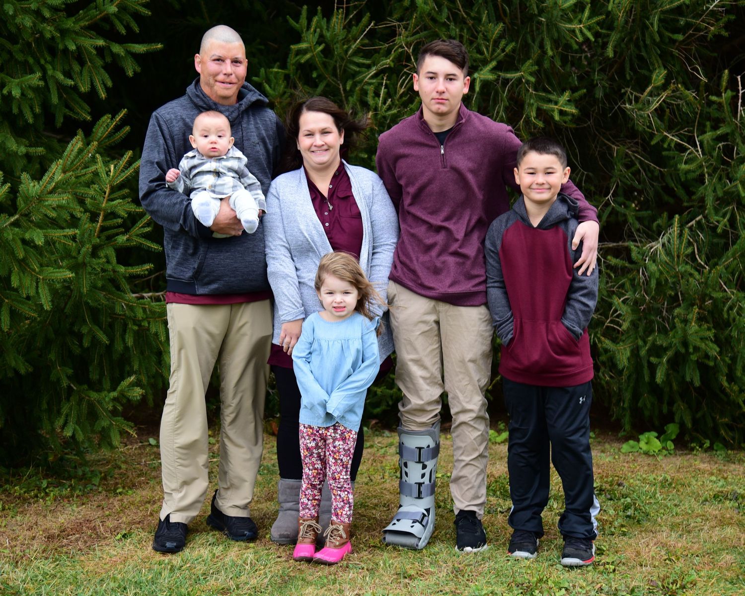 Multi-generational family group poses together outdoors with greenery in background.