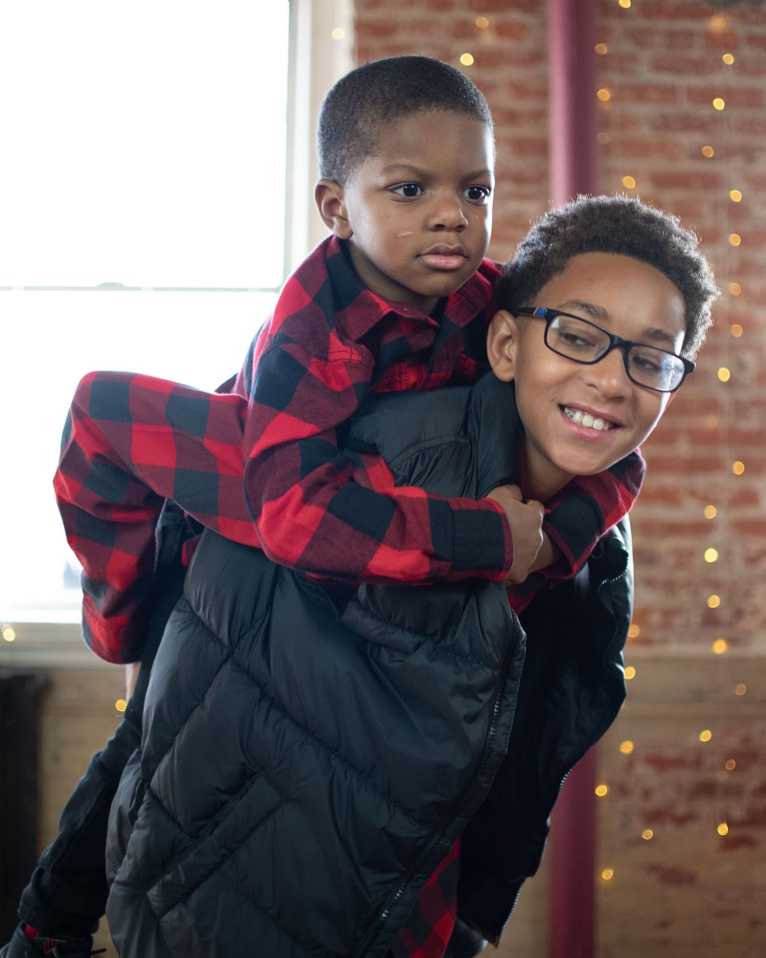 Children in winter coats and buffalo plaid patterns pose playfully indoors.