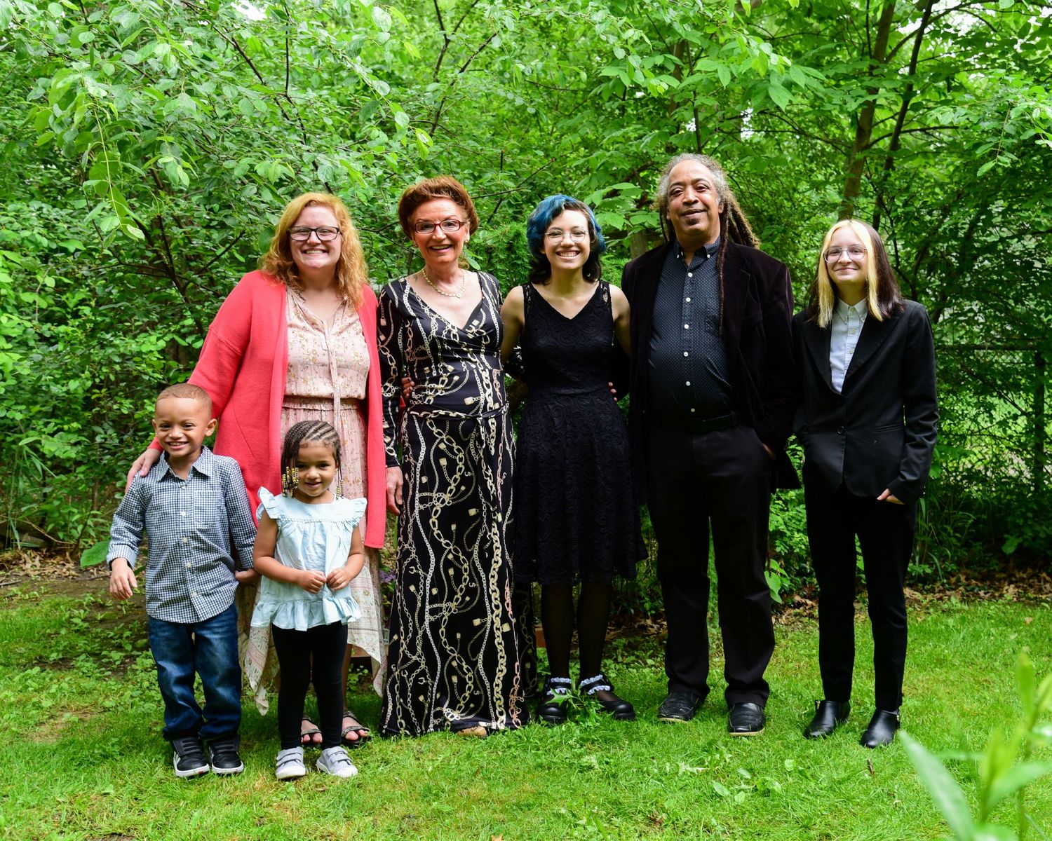 Line of people standing together against a backdrop of vibrant green foliage in a park setting.