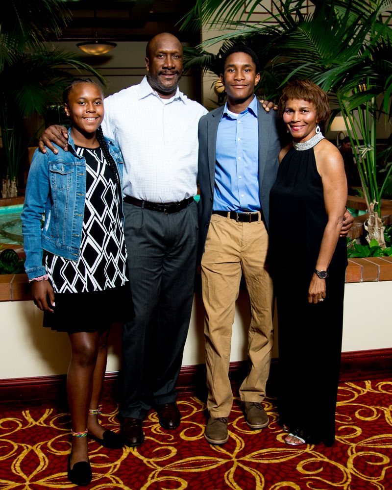Family group in coordinated business casual attire poses against ornate carpet and indoor setting.
