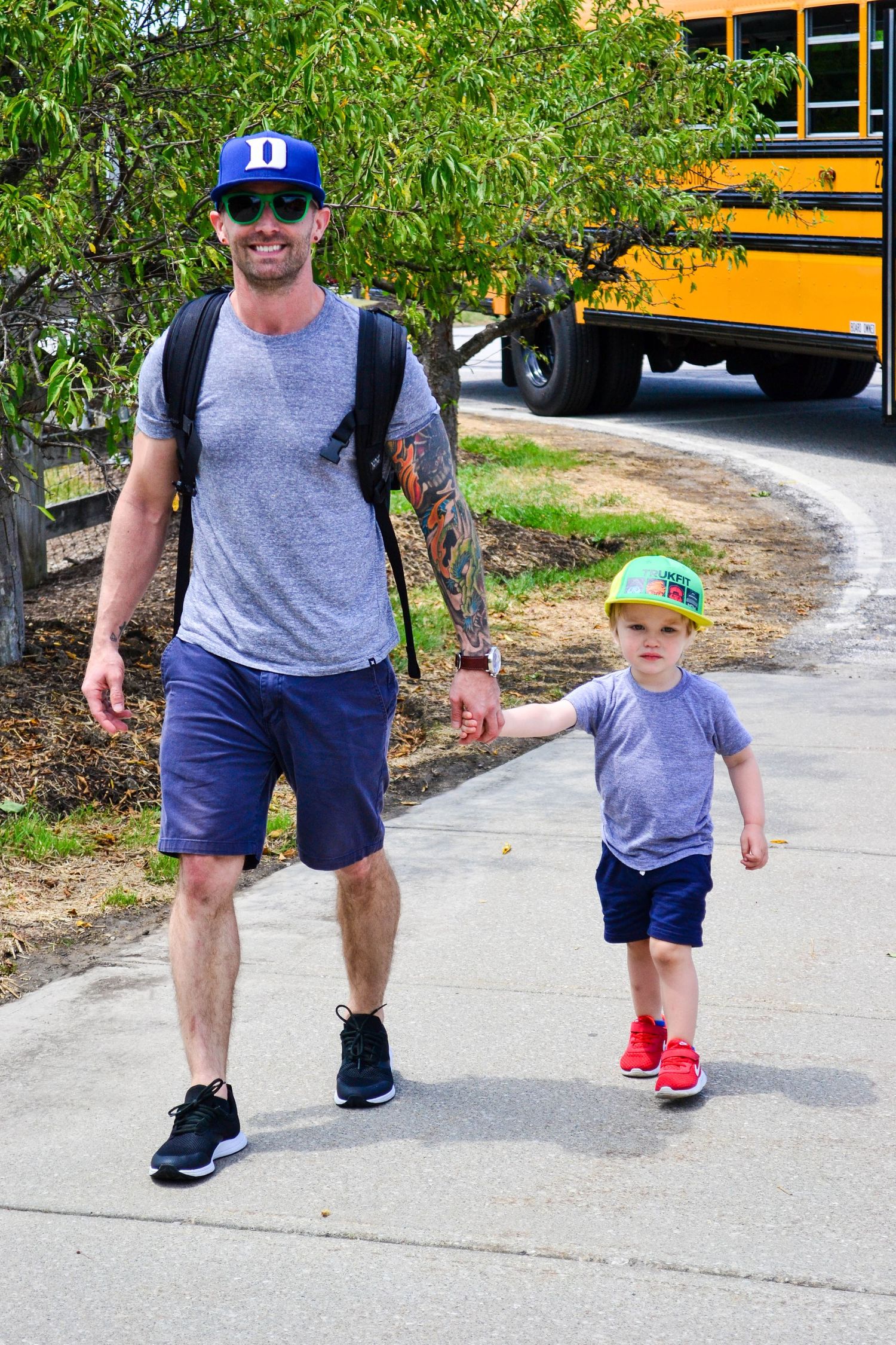 Parent and child walking together on sidewalk near yellow school bus wearing matching outfits.