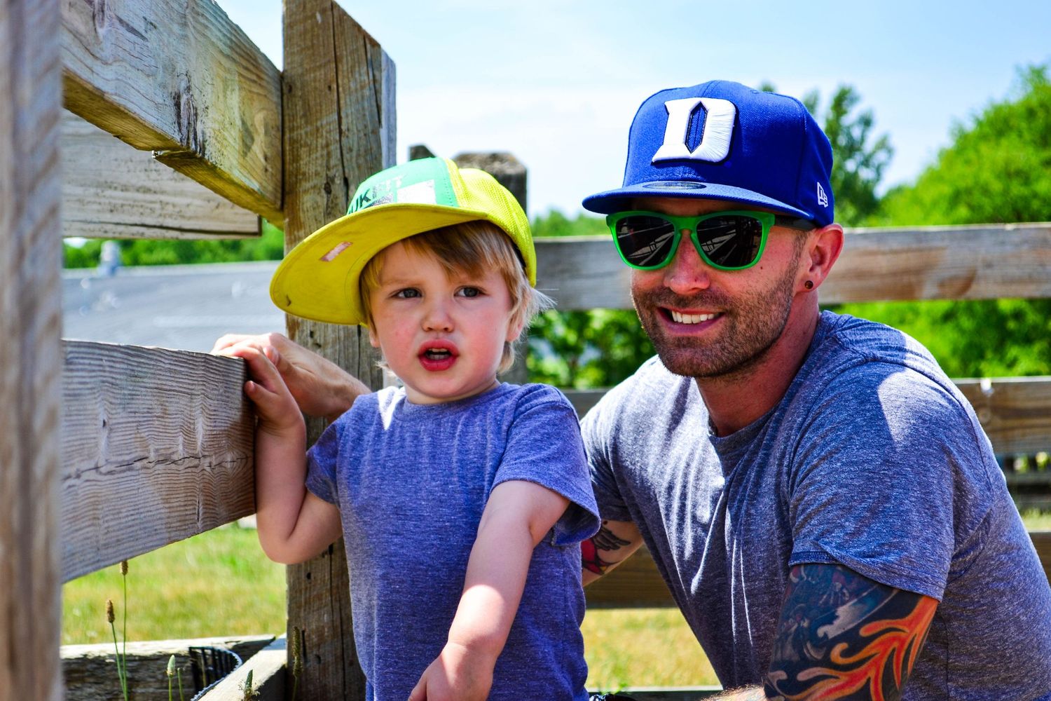 Children wearing baseball caps and sunglasses sit together outdoors on a sunny day.