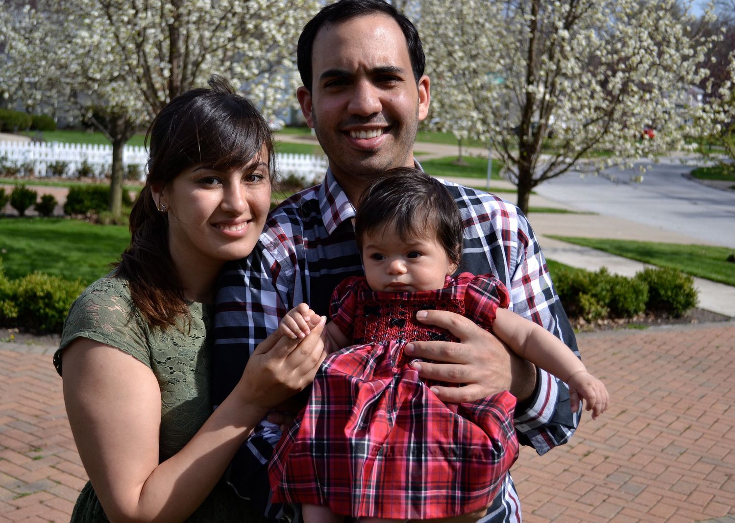 Family members embrace and smile together outdoors with blooming trees in the background.