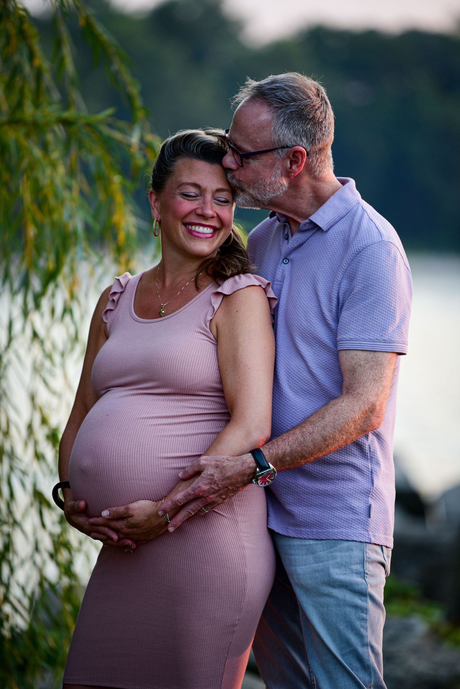Intimate maternity portraits captured in nature with soft lighting and willow tree backdrop.