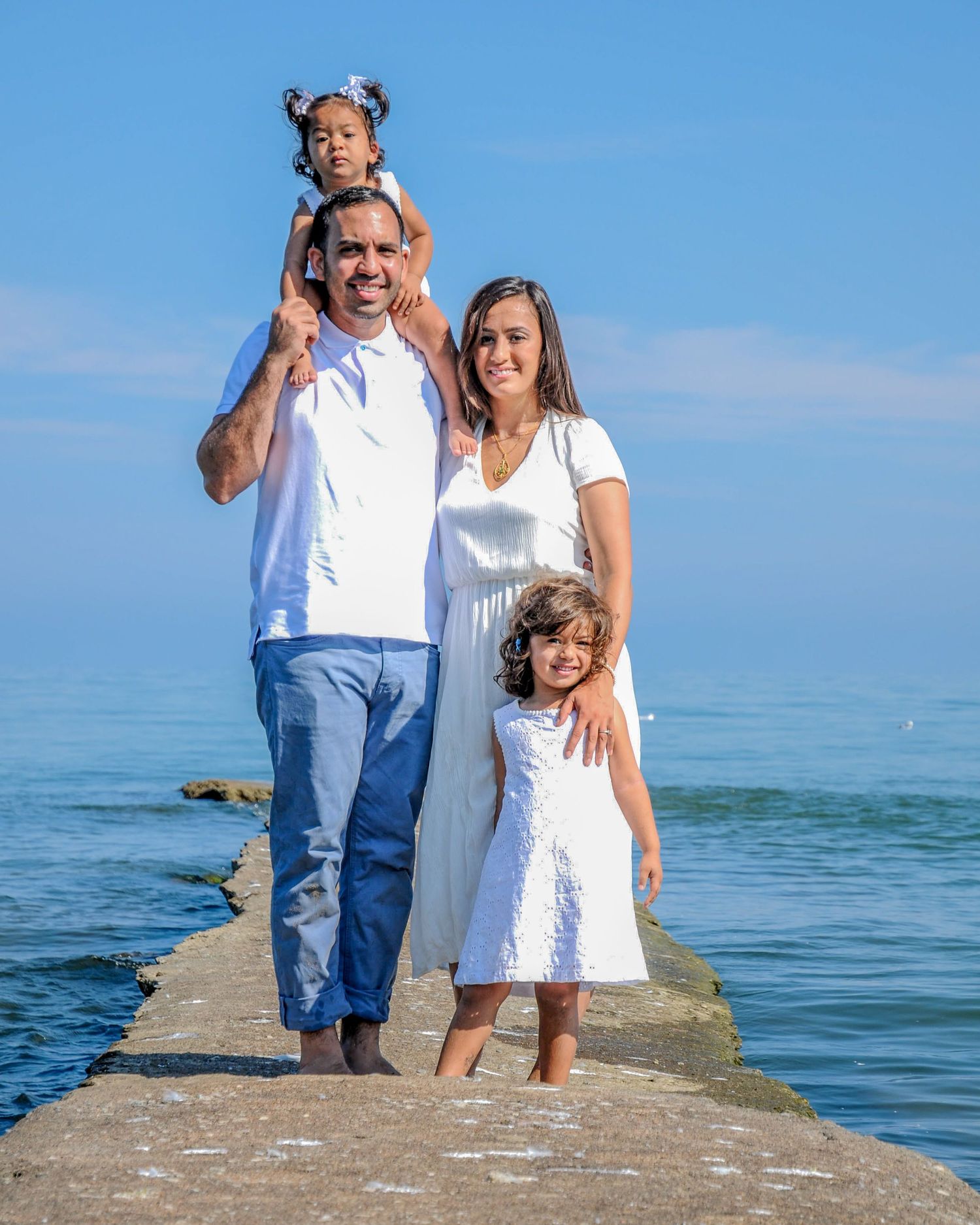 Family members pose together on a concrete pier extending into calm blue ocean waters.