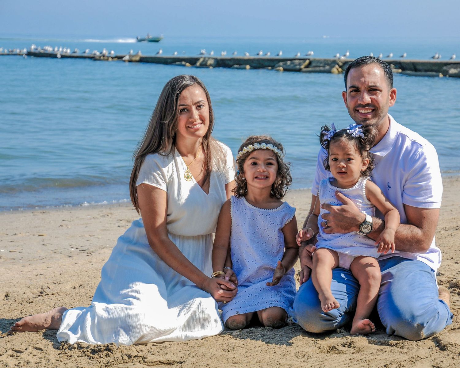 Family portrait session at the beach with harbor and boats visible in the background.