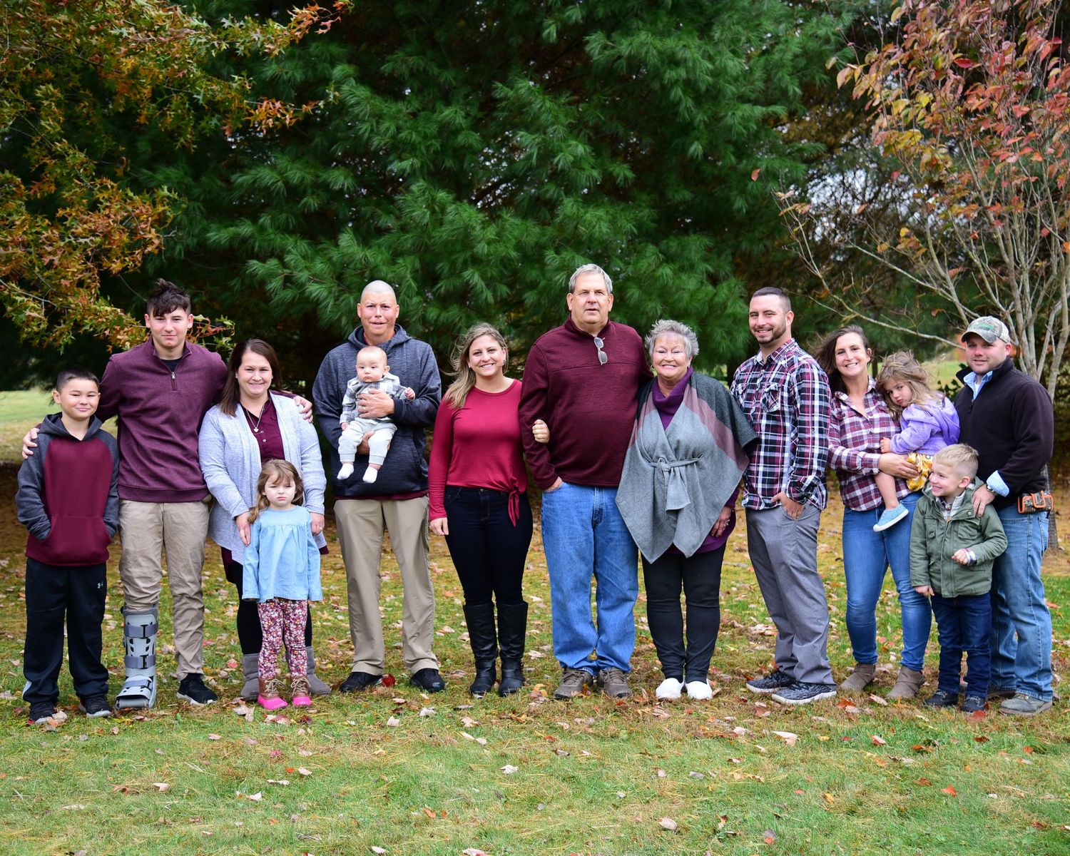 Large group of people lined up outdoors in autumn setting with colorful fall foliage in background.