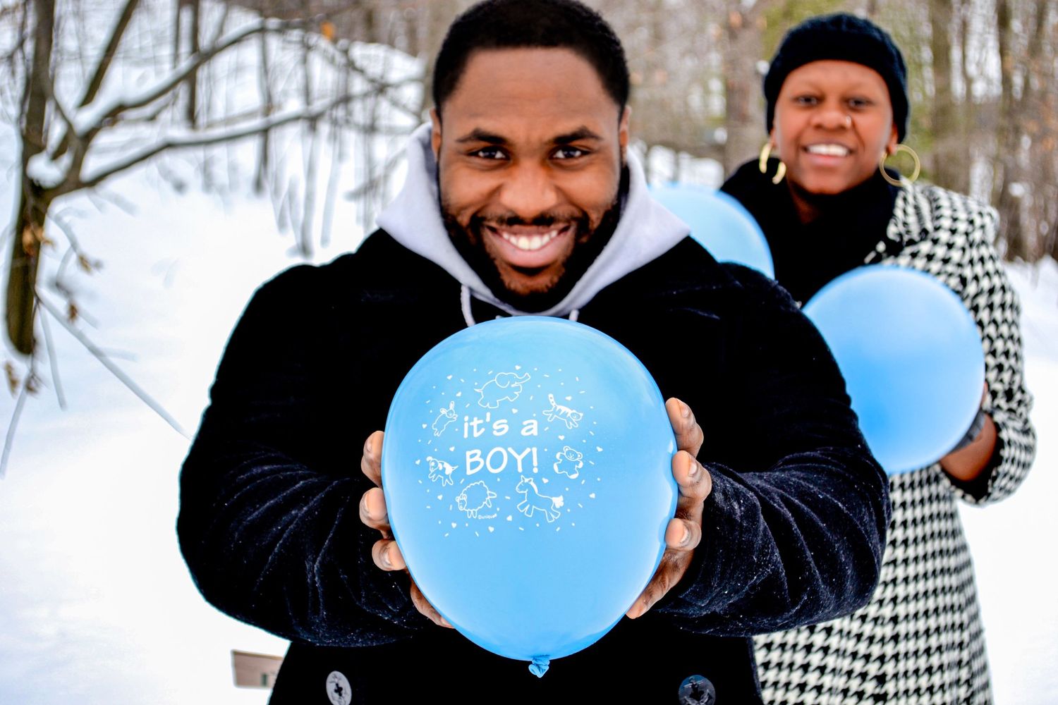 Winter photo shoot with blue gender reveal balloons in snowy setting.