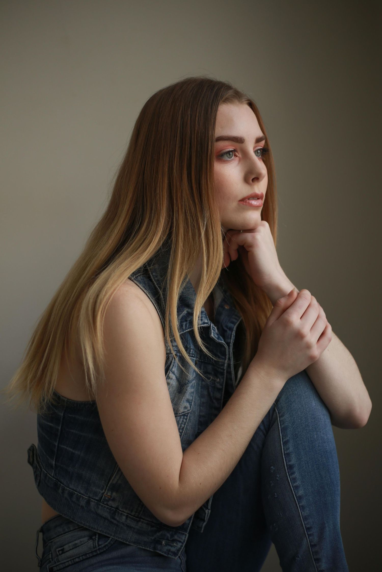 Thoughtful portrait of someone in denim sitting in contemplative pose against neutral background.
