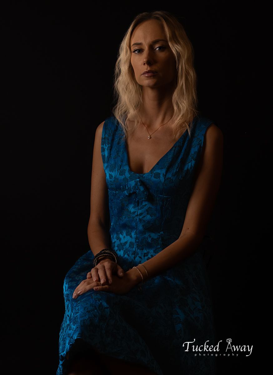 Dramatic low-key portrait in a blue velvet dress against dark background.