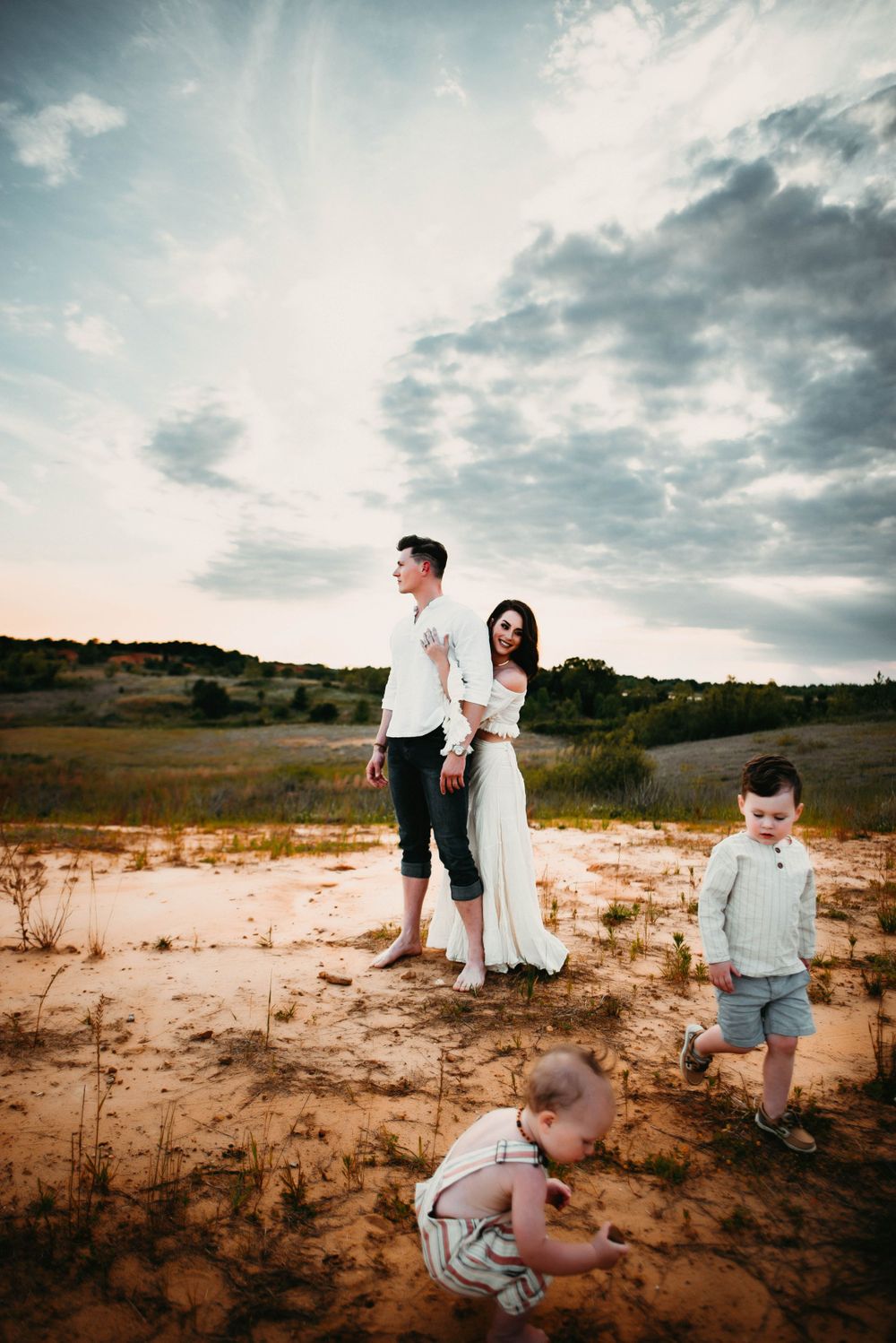 Family playing together on sandy terrain under dramatic cloudy sky at sunset.