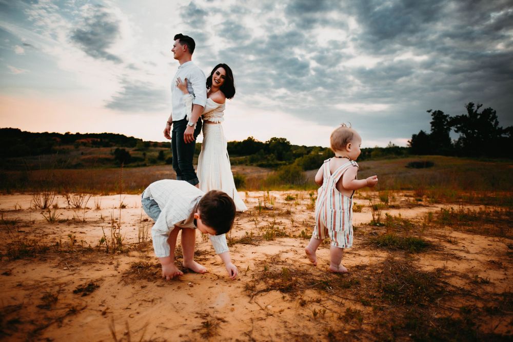 Family enjoying playful moments on sandy ground during golden hour.