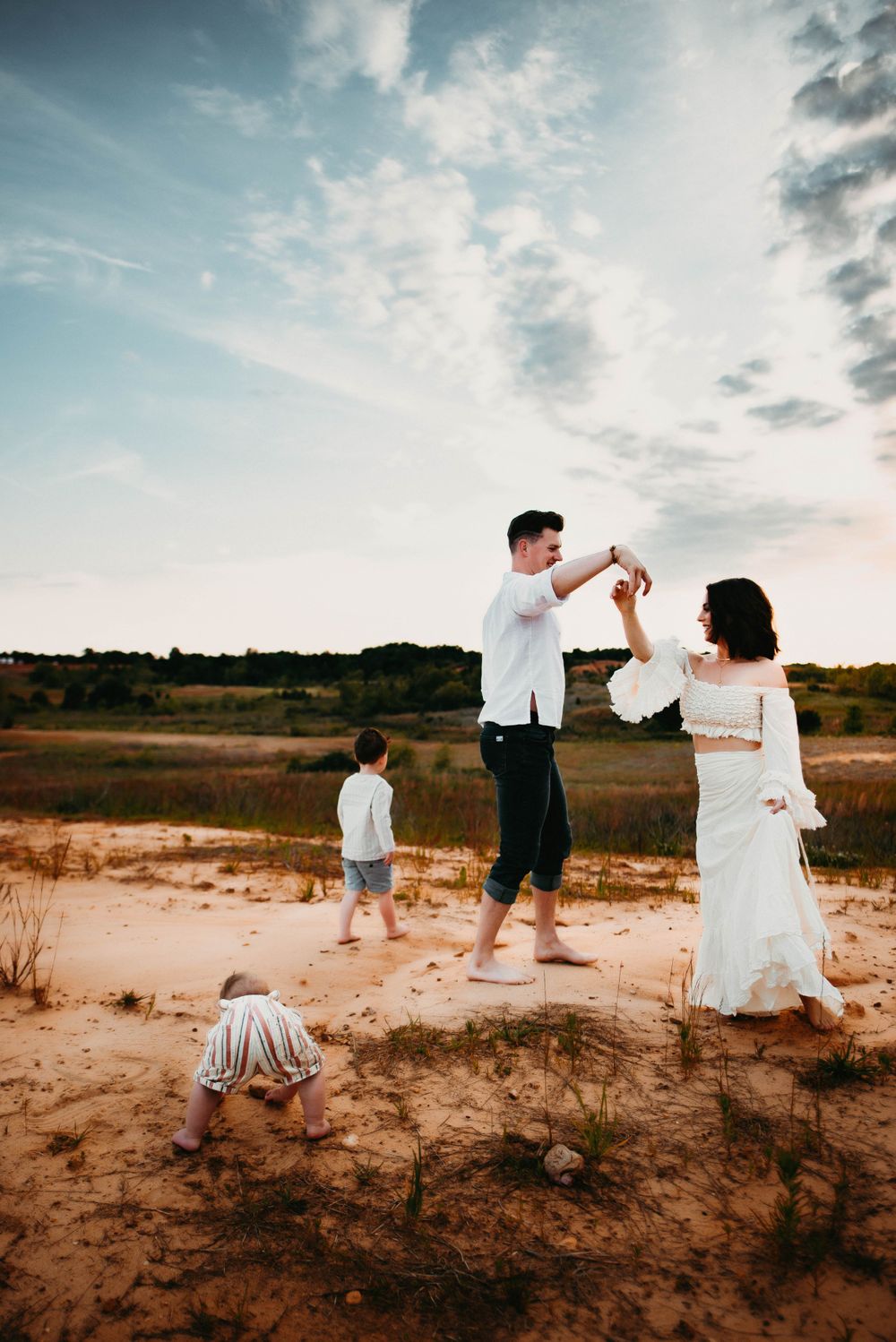 Family playing and walking together on sandy terrain at dusk.