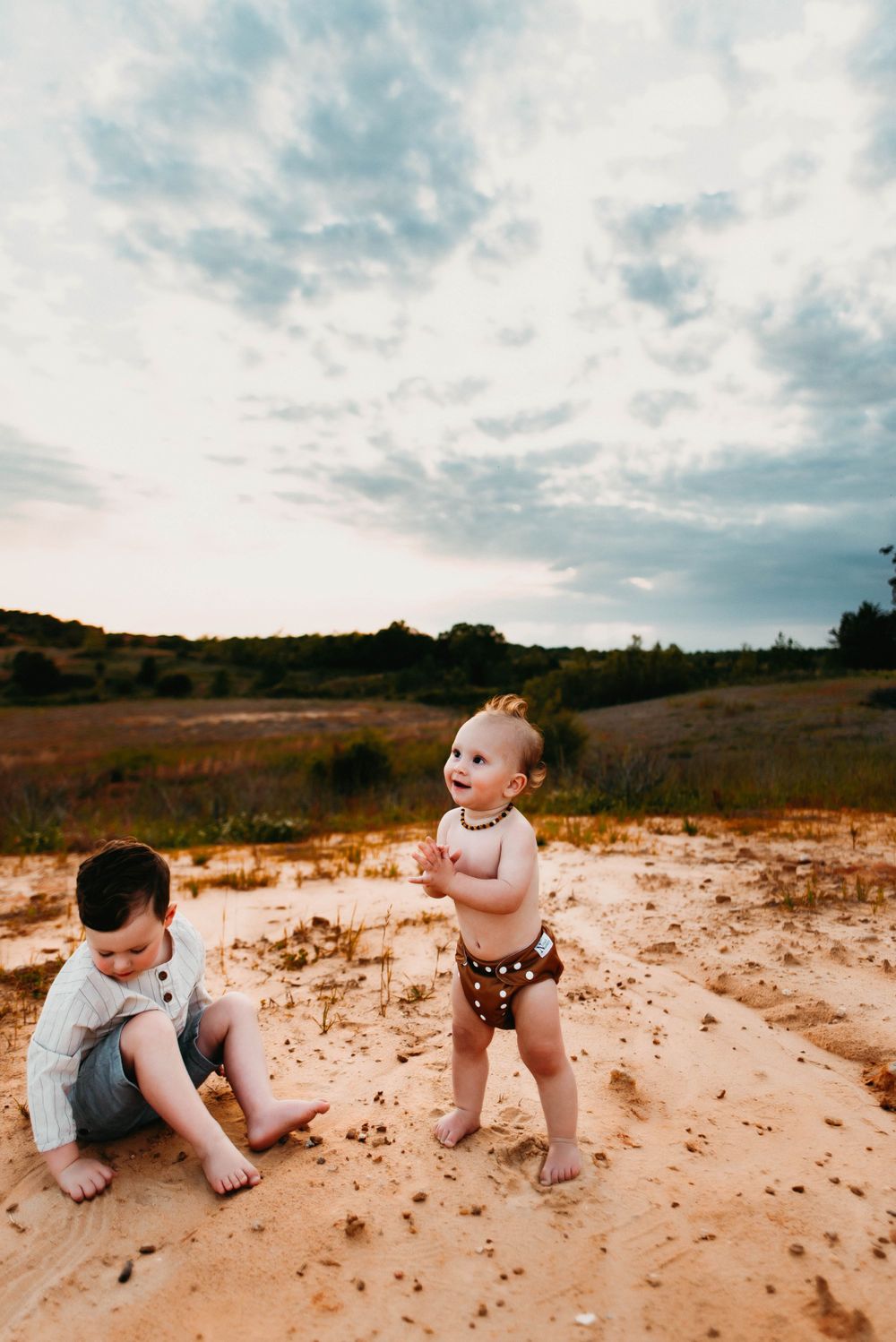 Toddlers crawling and exploring sandy terrain under cloudy sky.