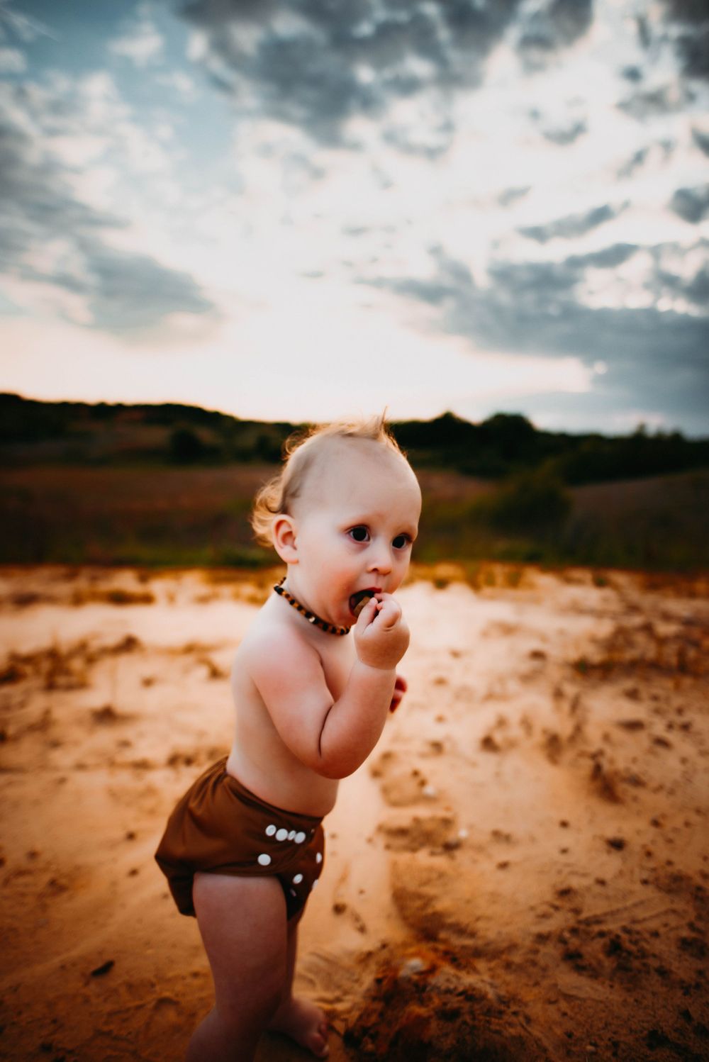 Toddler in brown diaper exploring sandy terrain during golden hour.