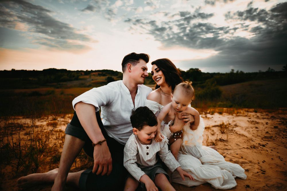 Family of four sits together on sandy ground during sunset photoshoot.